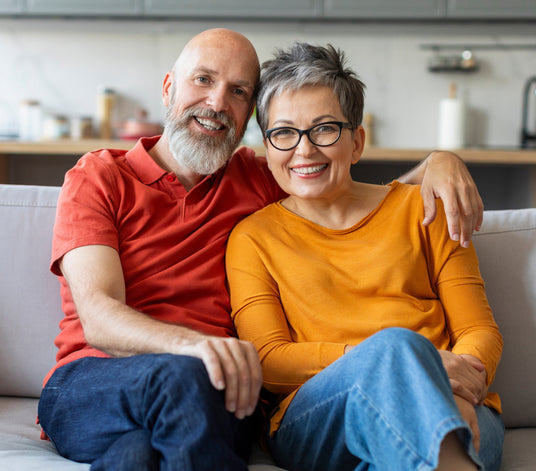 Smilende ældre par sidder sammen i sofaen hos Seniorshop.dk